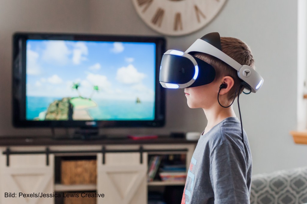 Ein Junge mit einem VR-Set spielt Playstation. Symbolbild für IT-Sicherheit und Digitalisierung.