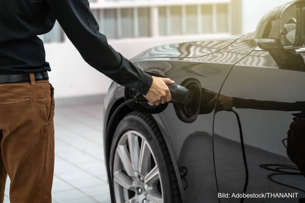 Person hat die Hand am Ladestecker eines Elektroautos. Die fliegen aus dem kommenden Fünfjahresplan der chinesischen Regierung.